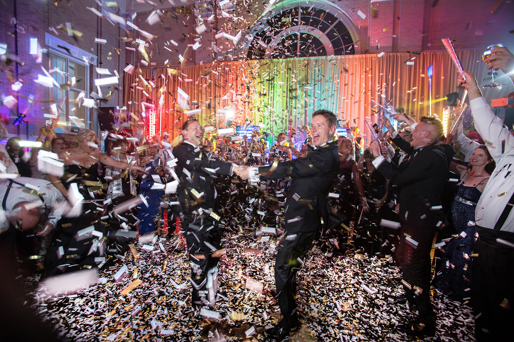 A lively wedding dance floor erupts in a colorful celebration as guests and newlyweds are surrounded by a cascade of confetti, capturing the energy and joy of the night.